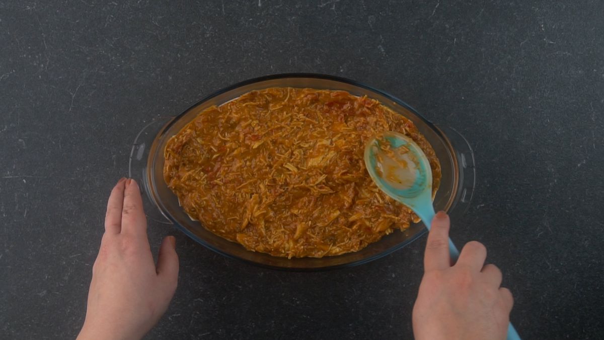 chicken mixture on top of tortillas in oval casserole dish