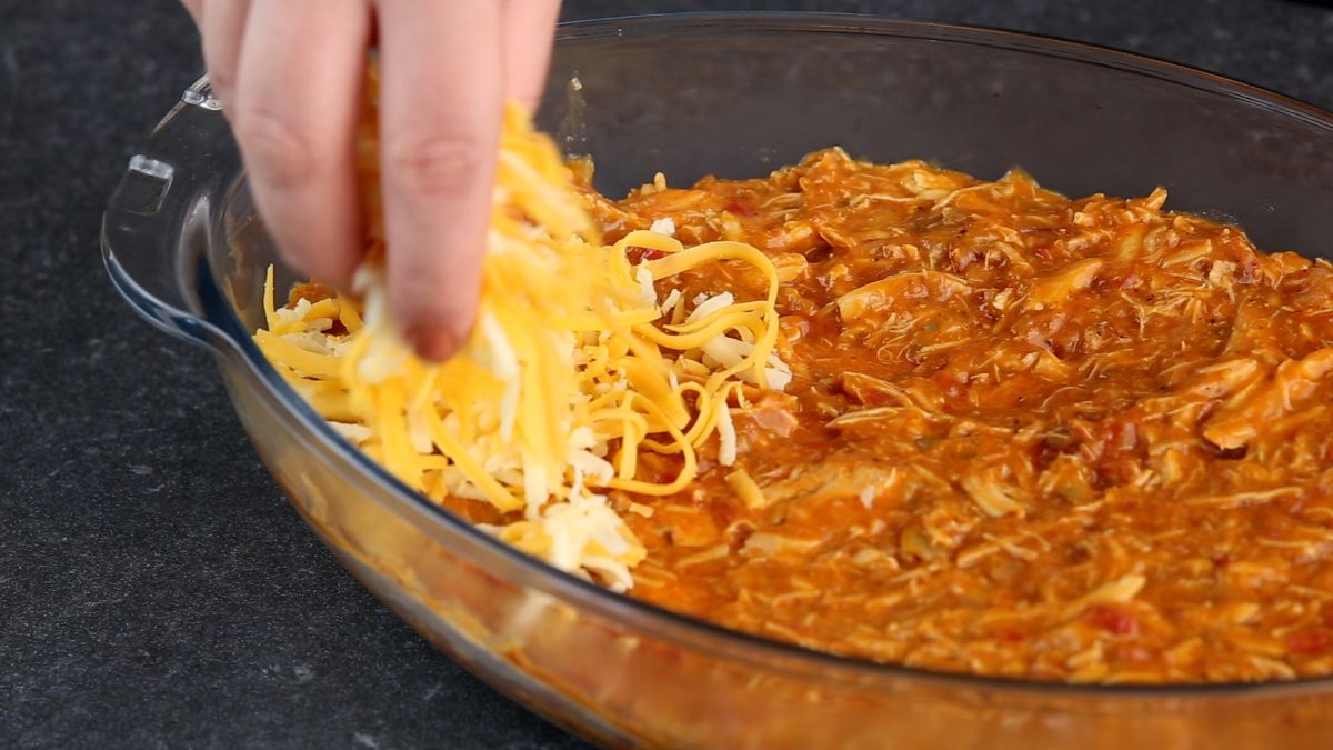 hand putting shredded cheese over top of casserole