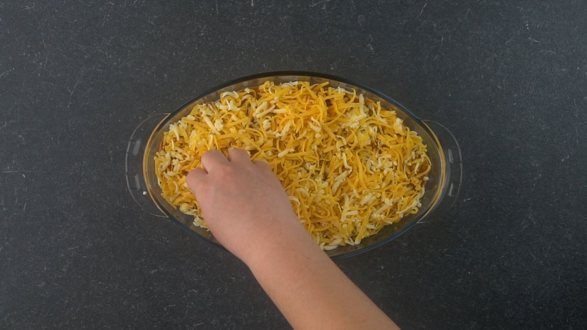 view looking down on cheese being sprinkled over oval casserole dish