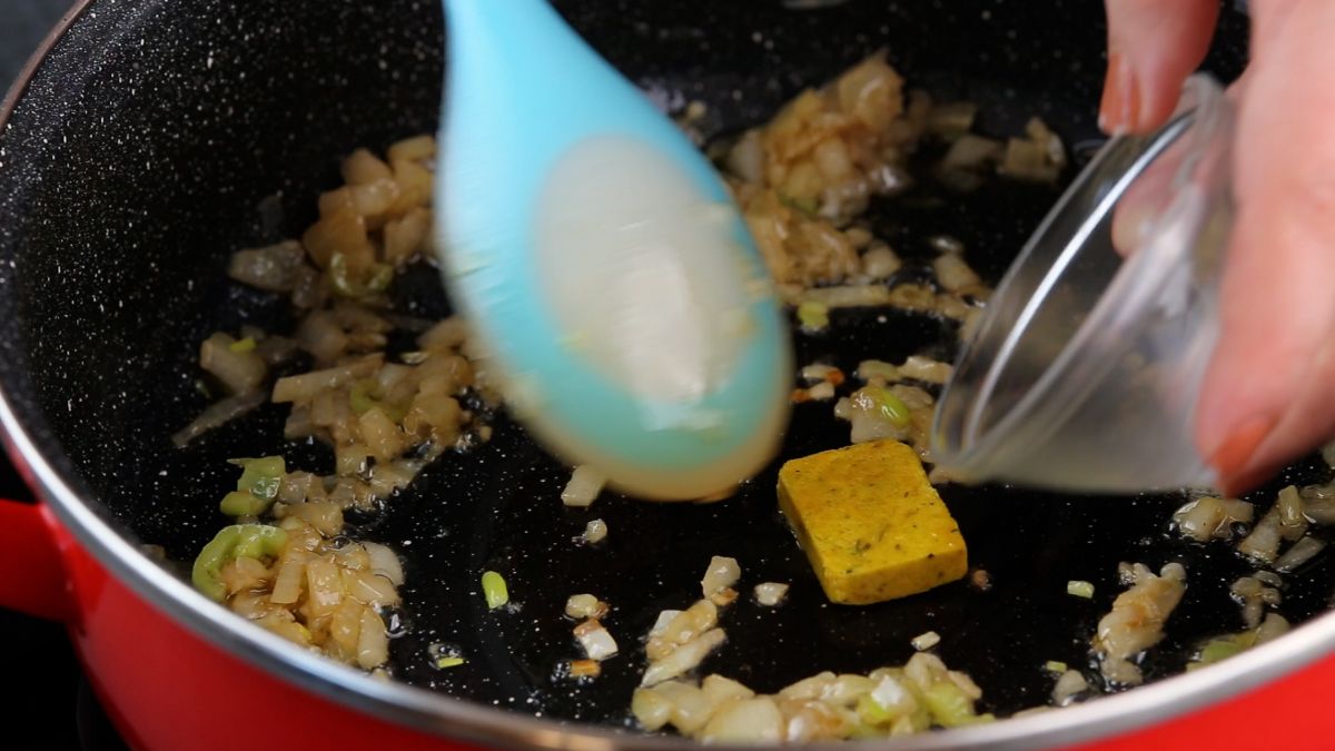spoon breaking up bouillon cube in skillet with vegetables