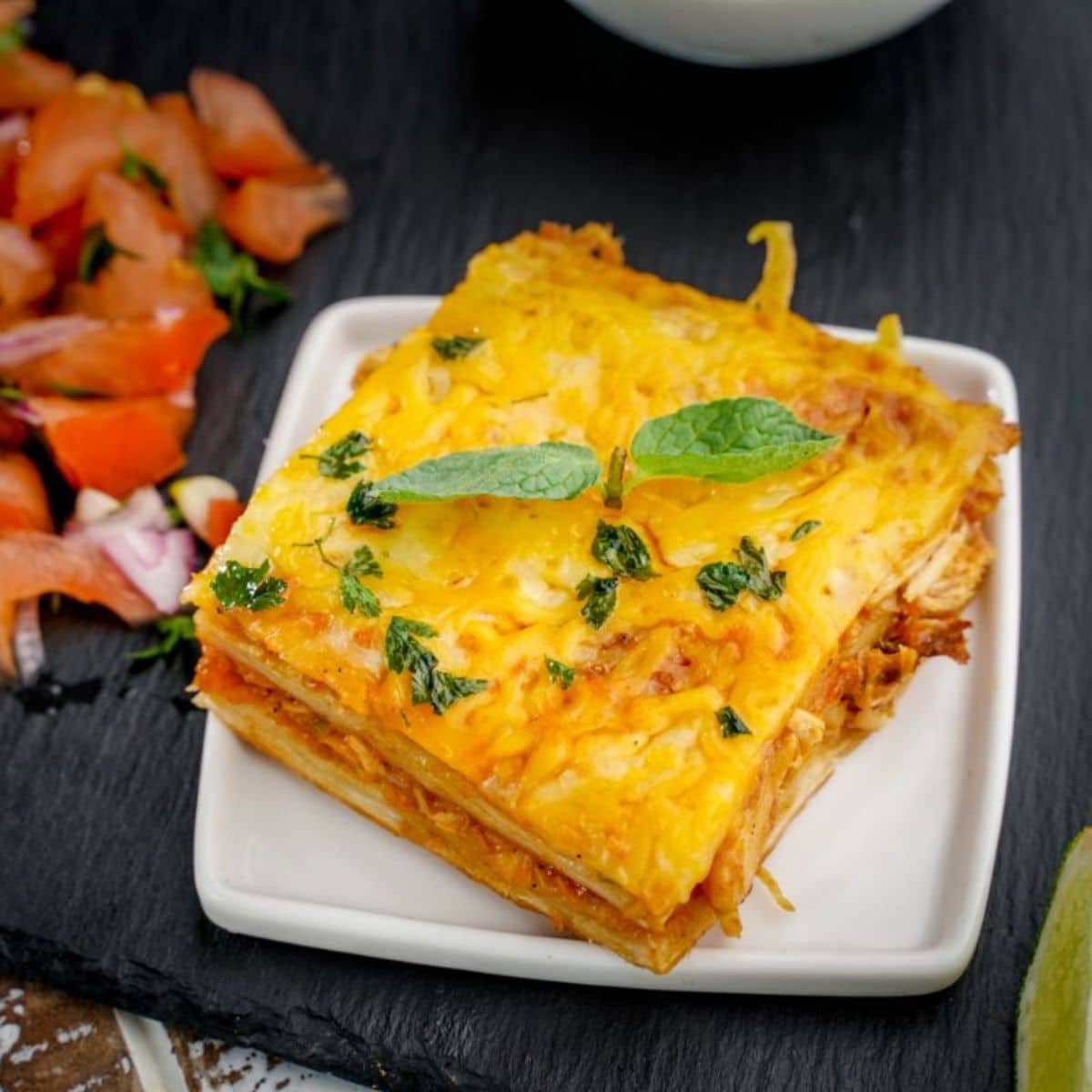 slice of casserole with cheese on top on square white plate on black table