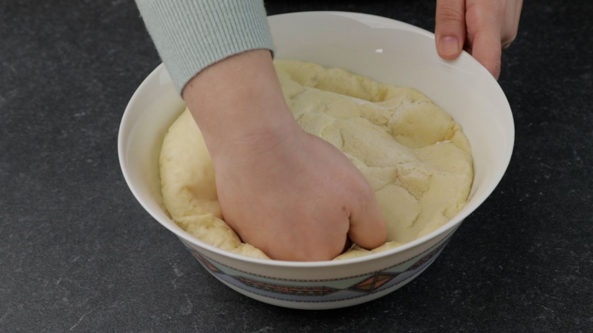 pizza dough in white bowl being punched down