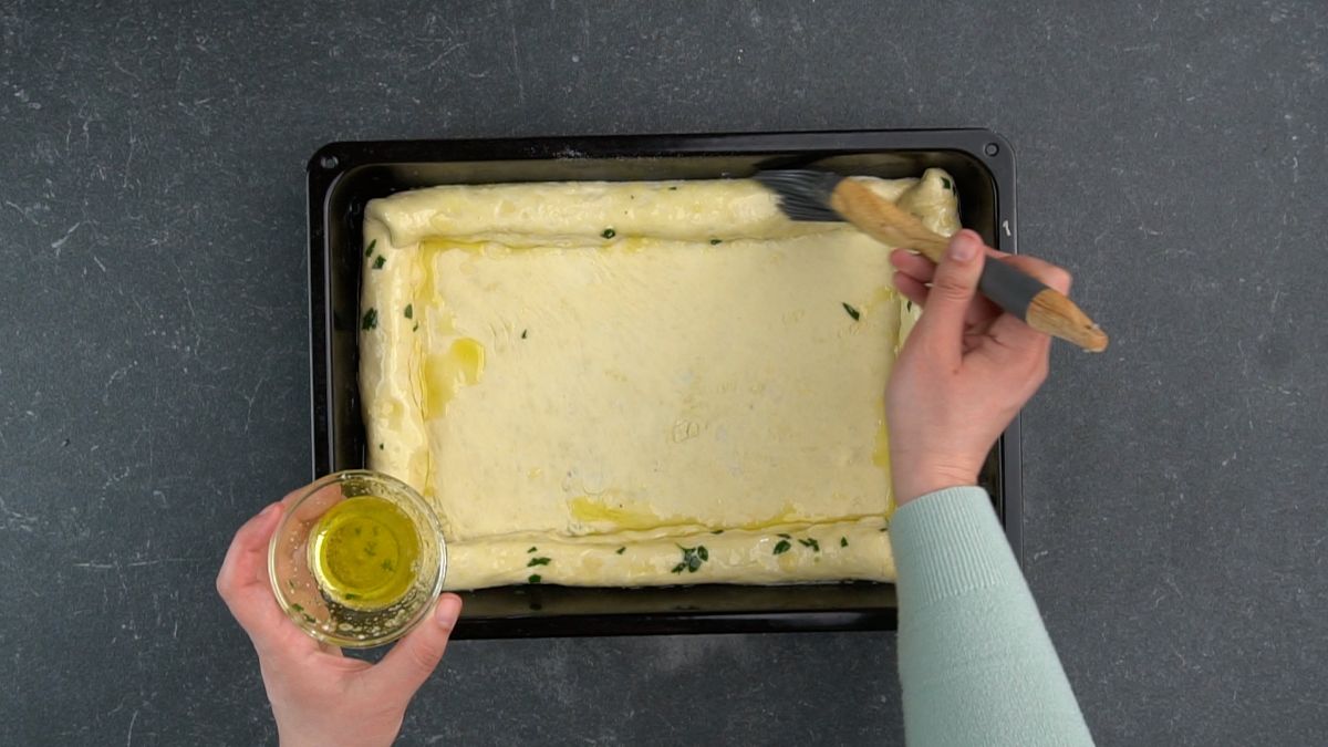 herbs and butter being brushed over edge of pizza