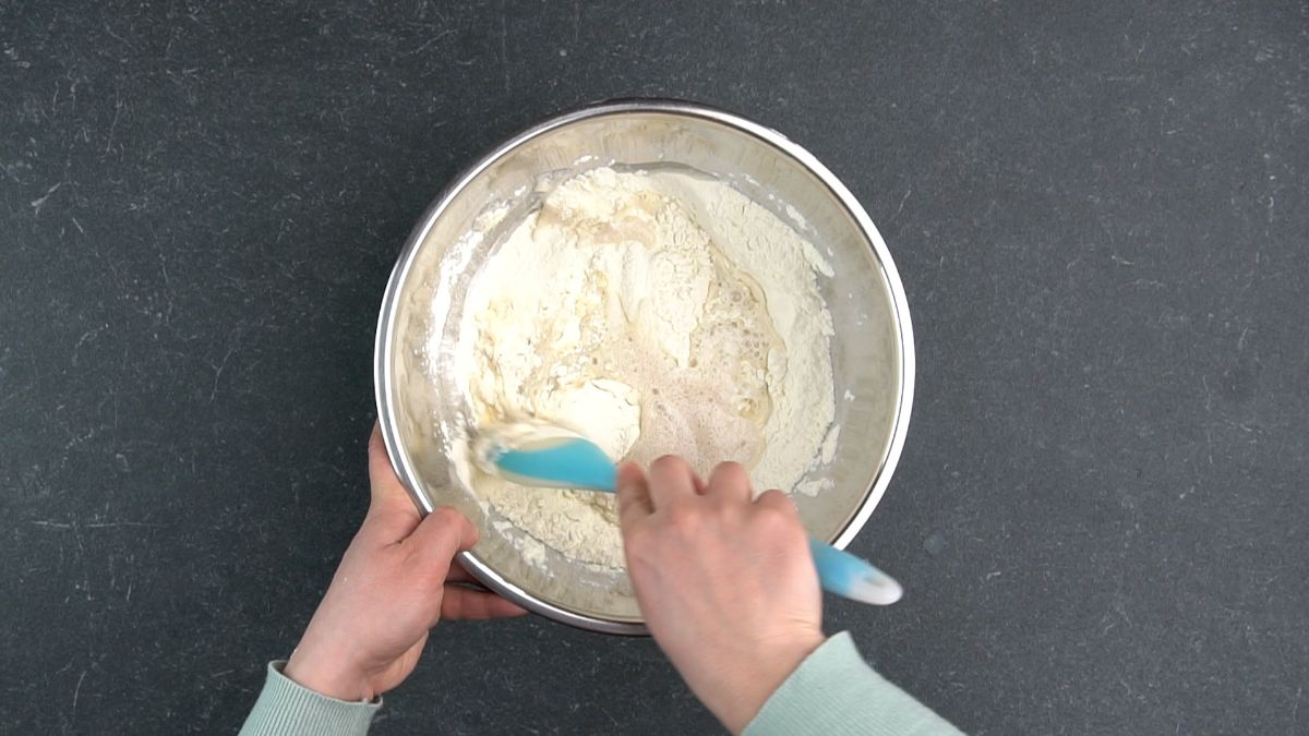 teal spoon being used to stir flour into dough