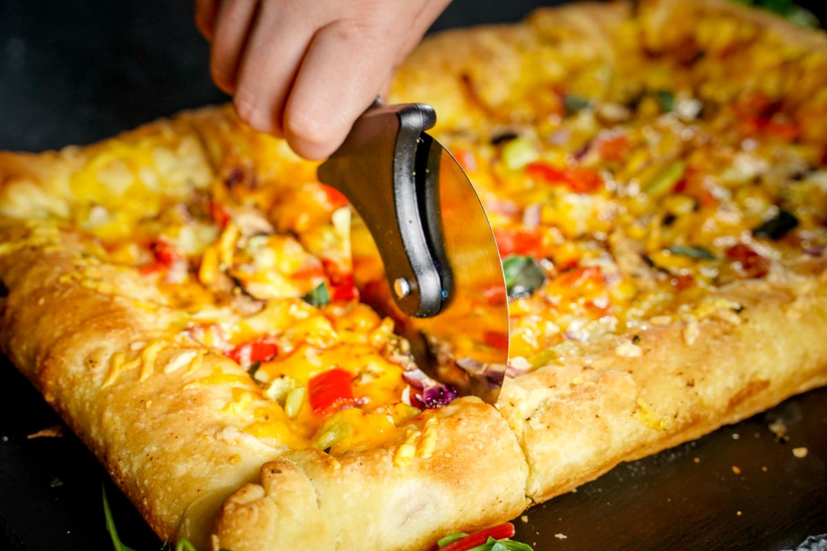 hand cutting veggie pizza with pizza cutter