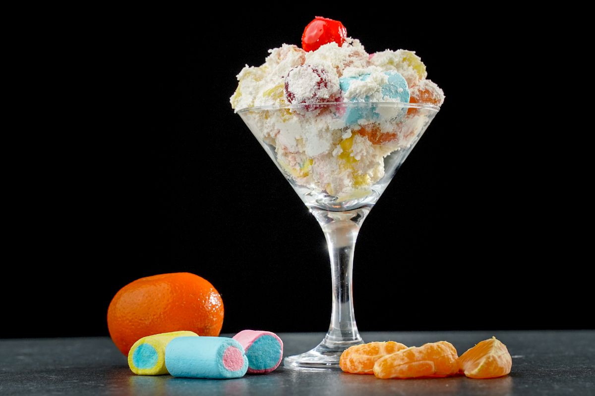 dessert glass of ambrosia salad on counter with marshmallows and orange slices with black background