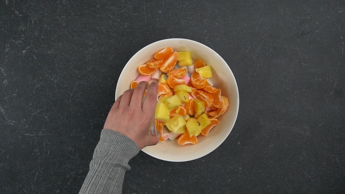hand pouring pineapple into bowl with orange slices