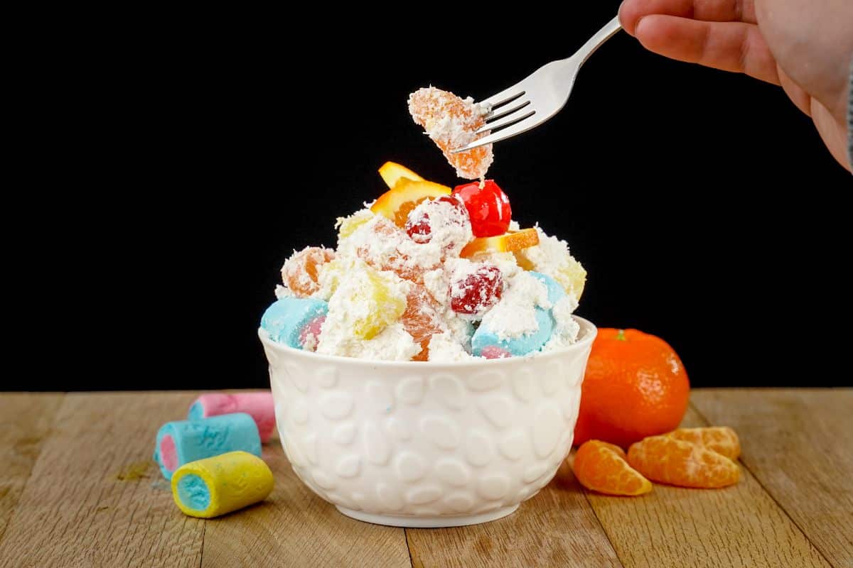 fork of fruit held above white bowl of ambrosia salad