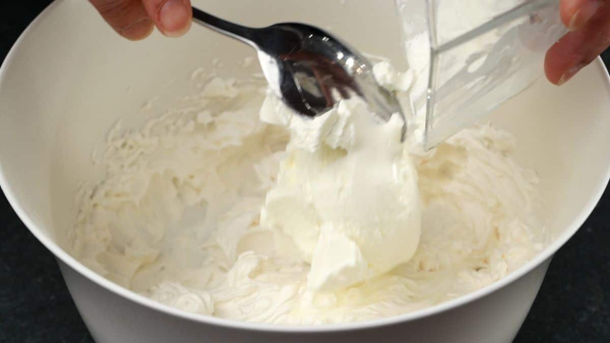 sour cream being added to white bowl of whipped cream