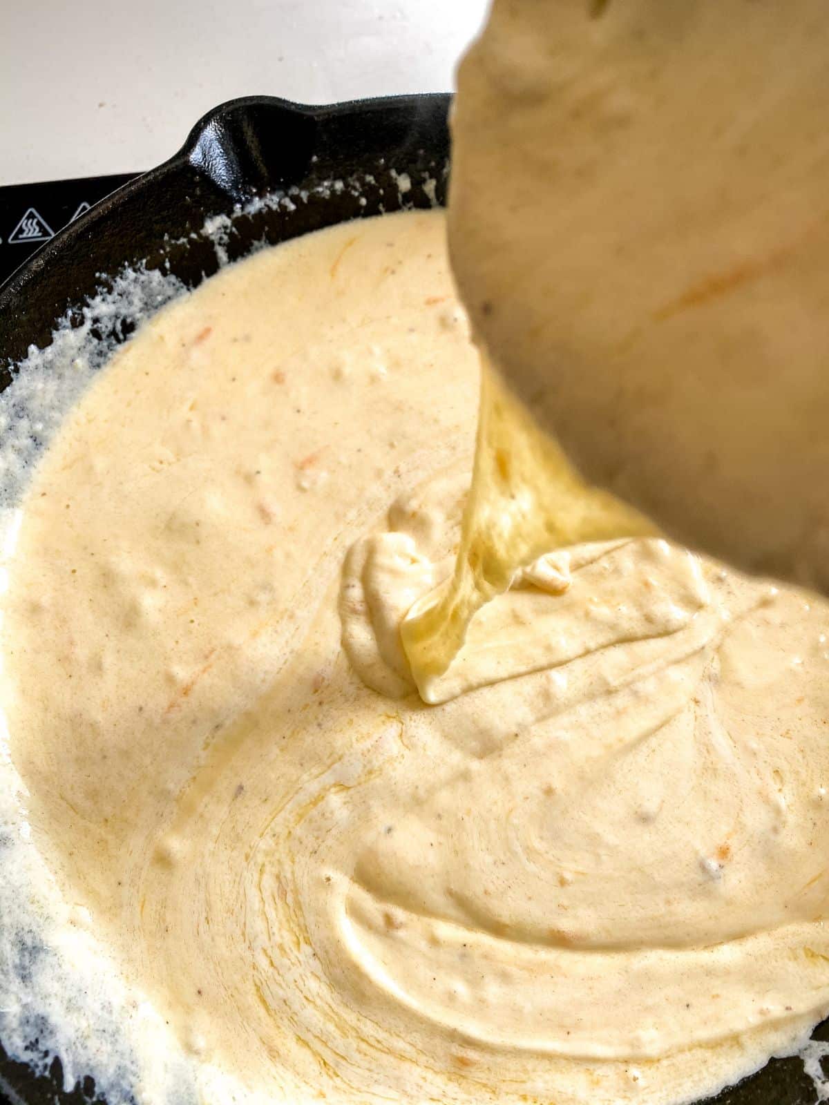 cheese sauce being poured into cast iron skillet