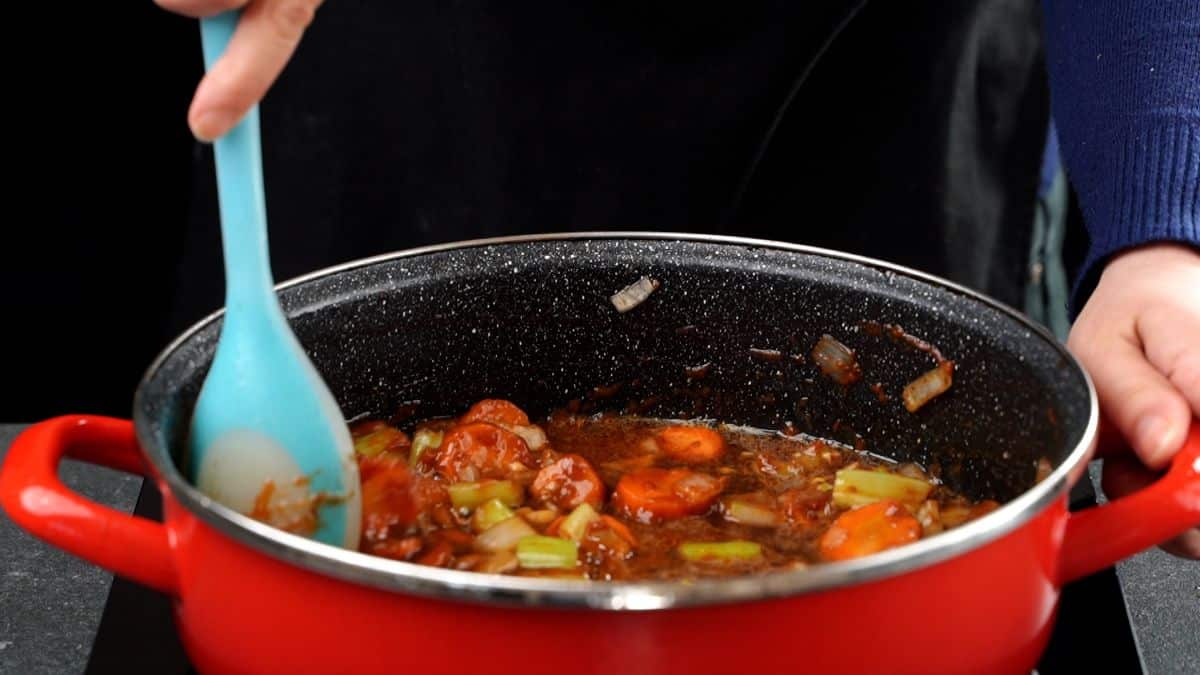 blue spoon stirring stew in red stockpot