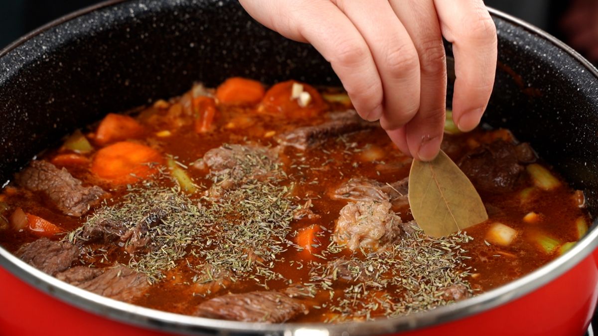 seasonings being added to beef stew in red pot