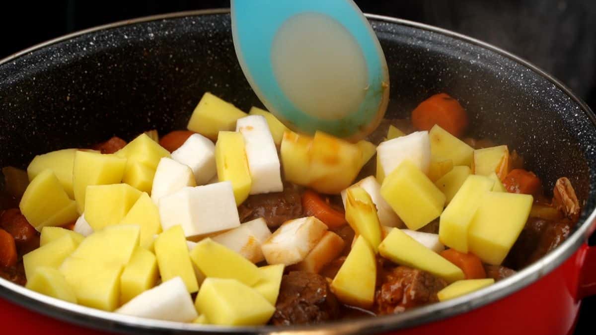 blue spoon stirring potatoes and turnips into stew