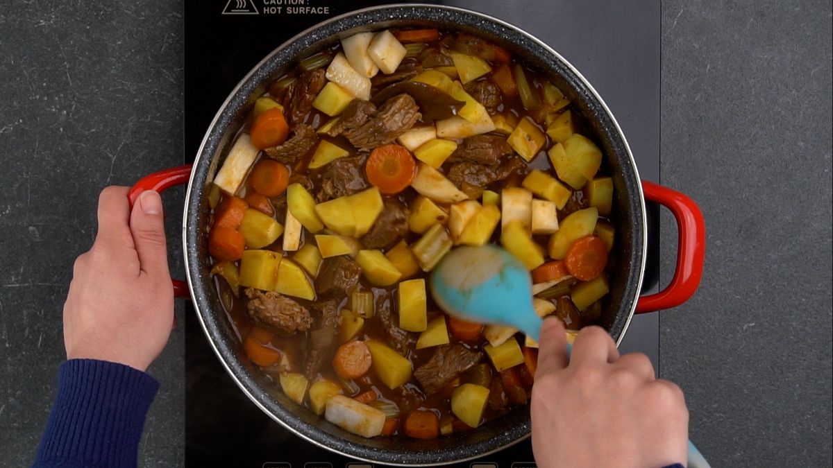 blue spoon stirring potatoes into stew