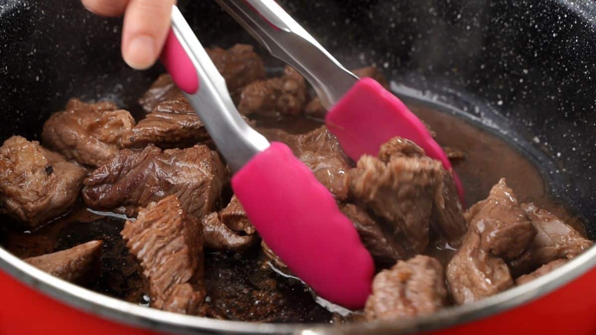 pink tongs removing beef from red skillet