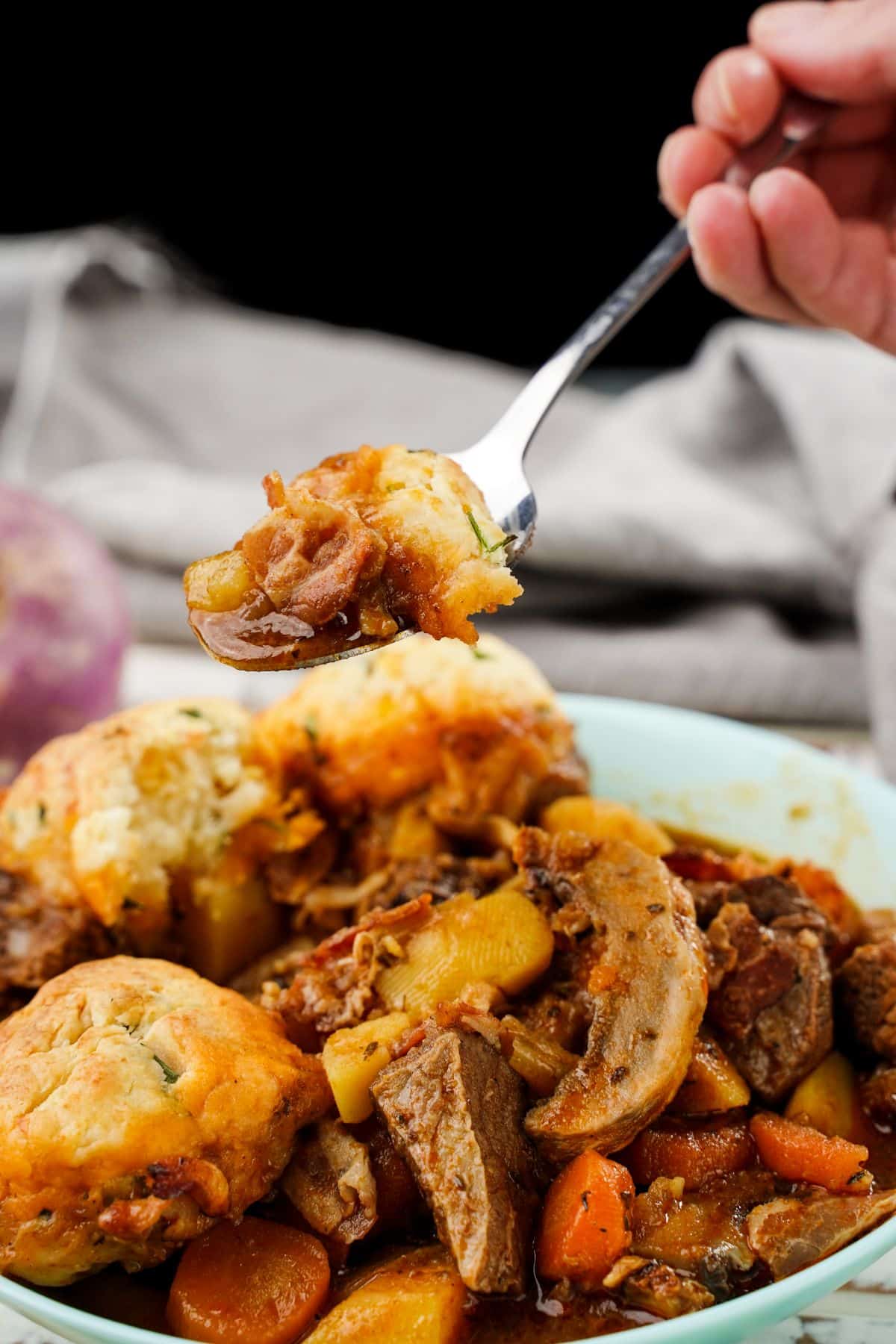 spoon of stew hovering above bowl topped by cheddar biscuits
