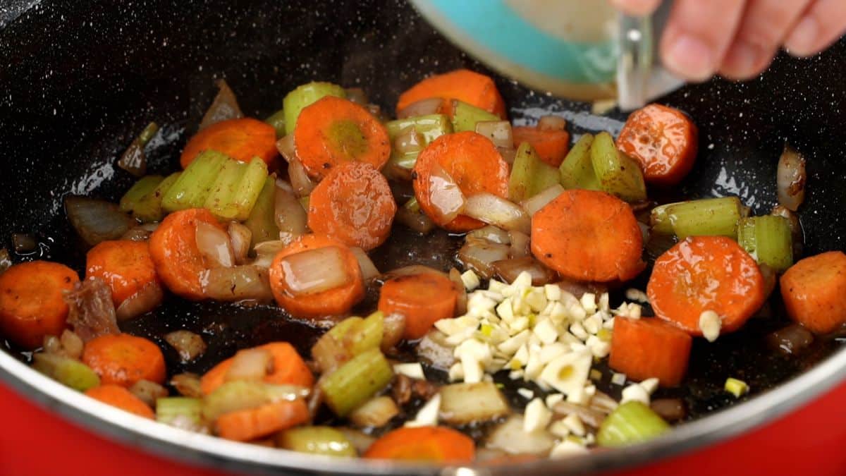 garlic being added to vegetables in stew pot