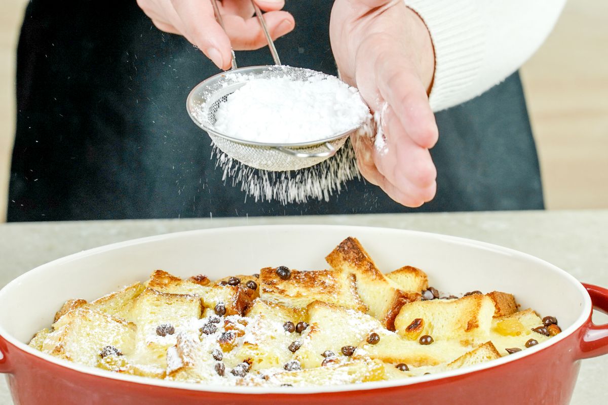 woman dusting top of bread pudding with powdered sugar