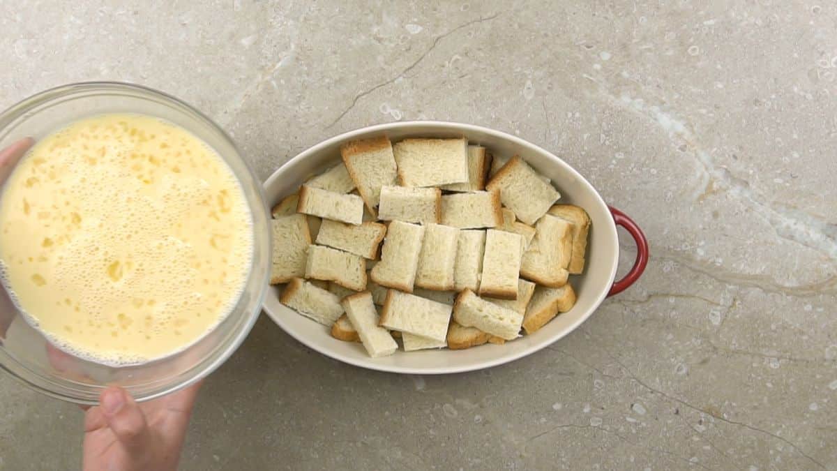custard being poured over bread in casserole dish