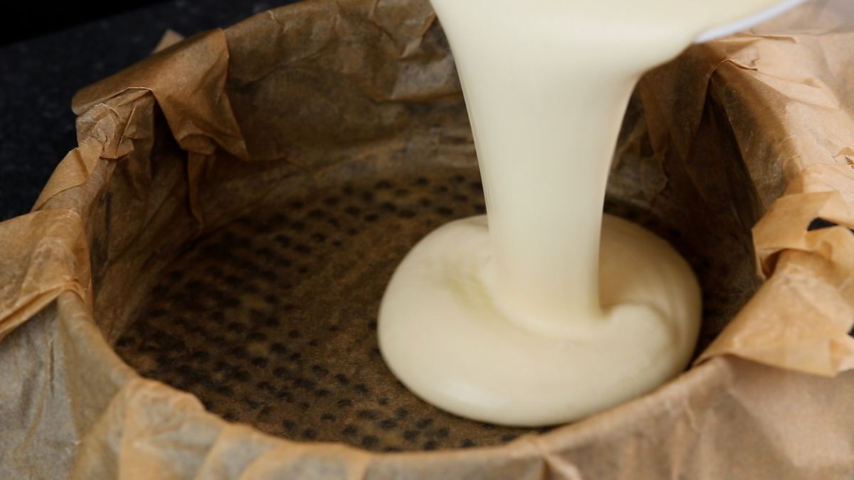 cheesecake batter being poured into parchment lined springform pan