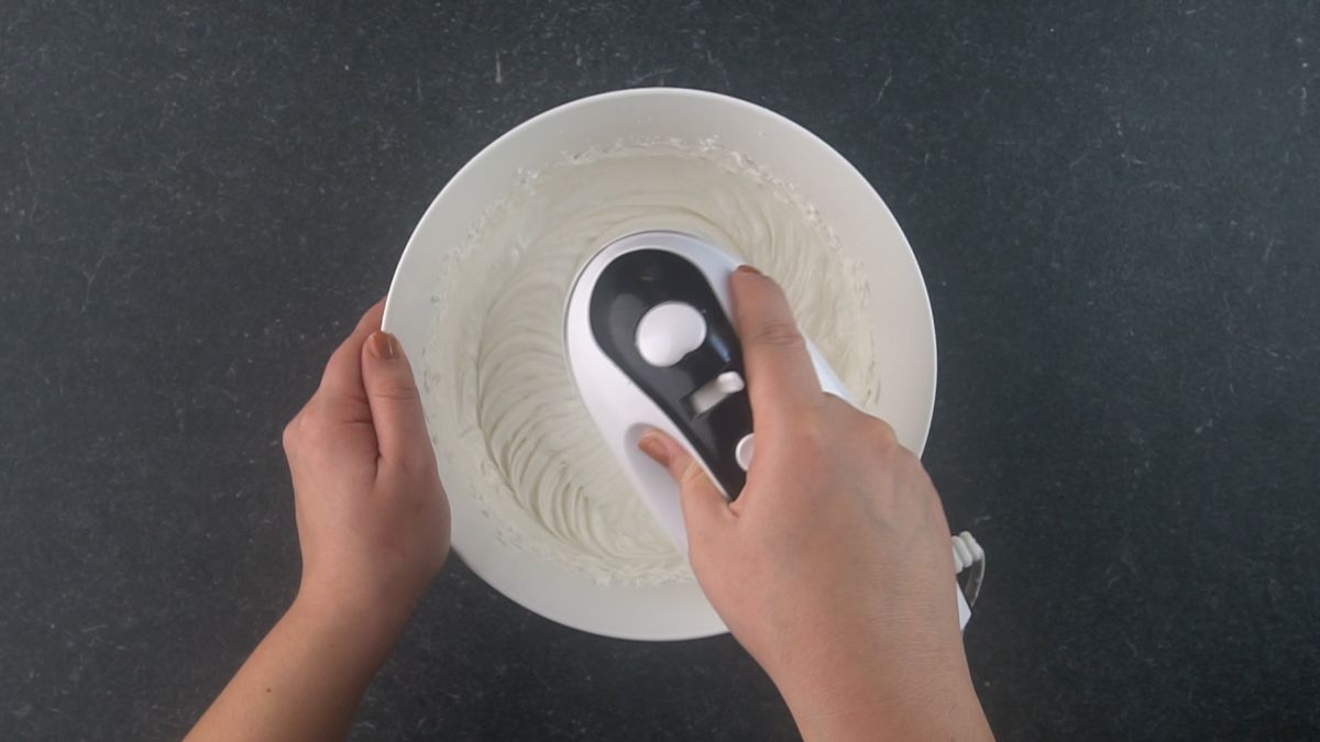 white bowl of cream cheese being beaten with electric mixer