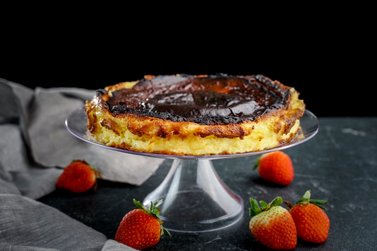 burnt basque cheesecake on glass cake stand on gray table with berries on table