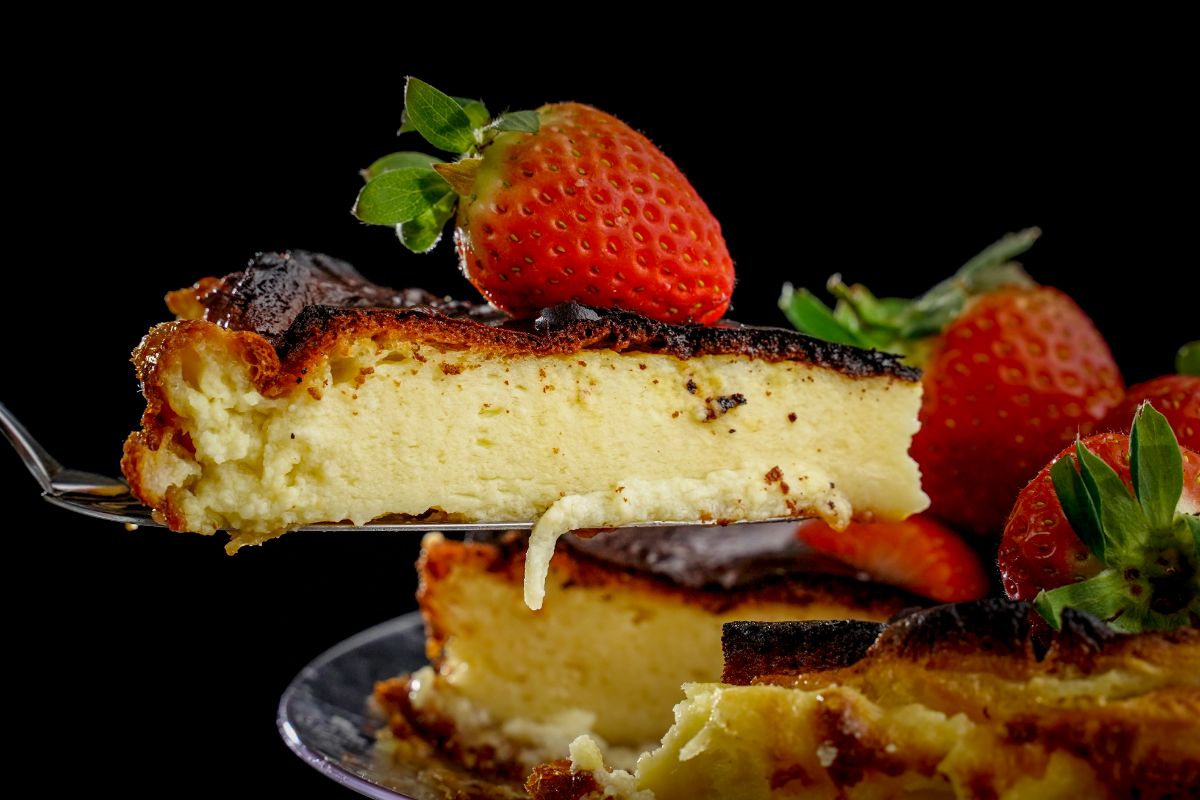 slice of cheesecake on spatula above cheesecake on stand