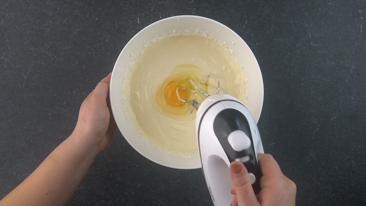 egg in bowl of creamed cream cheese with mixer