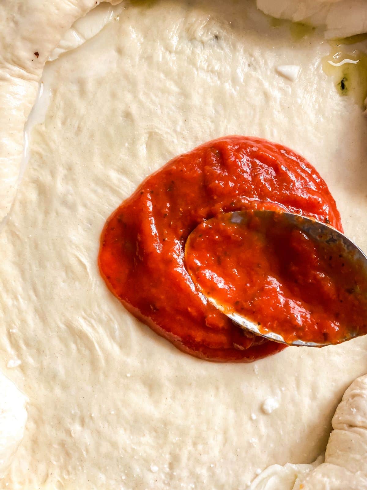 pizza sauce being spread over dough