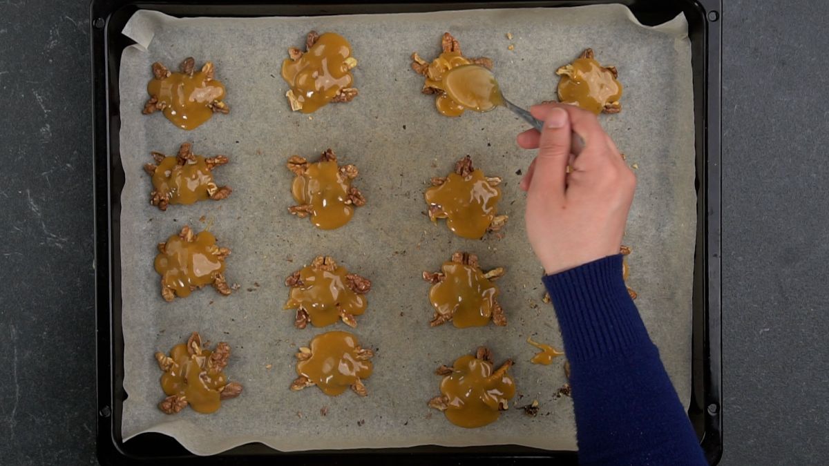 hand pouring caramel on top of walnut turtle pieces