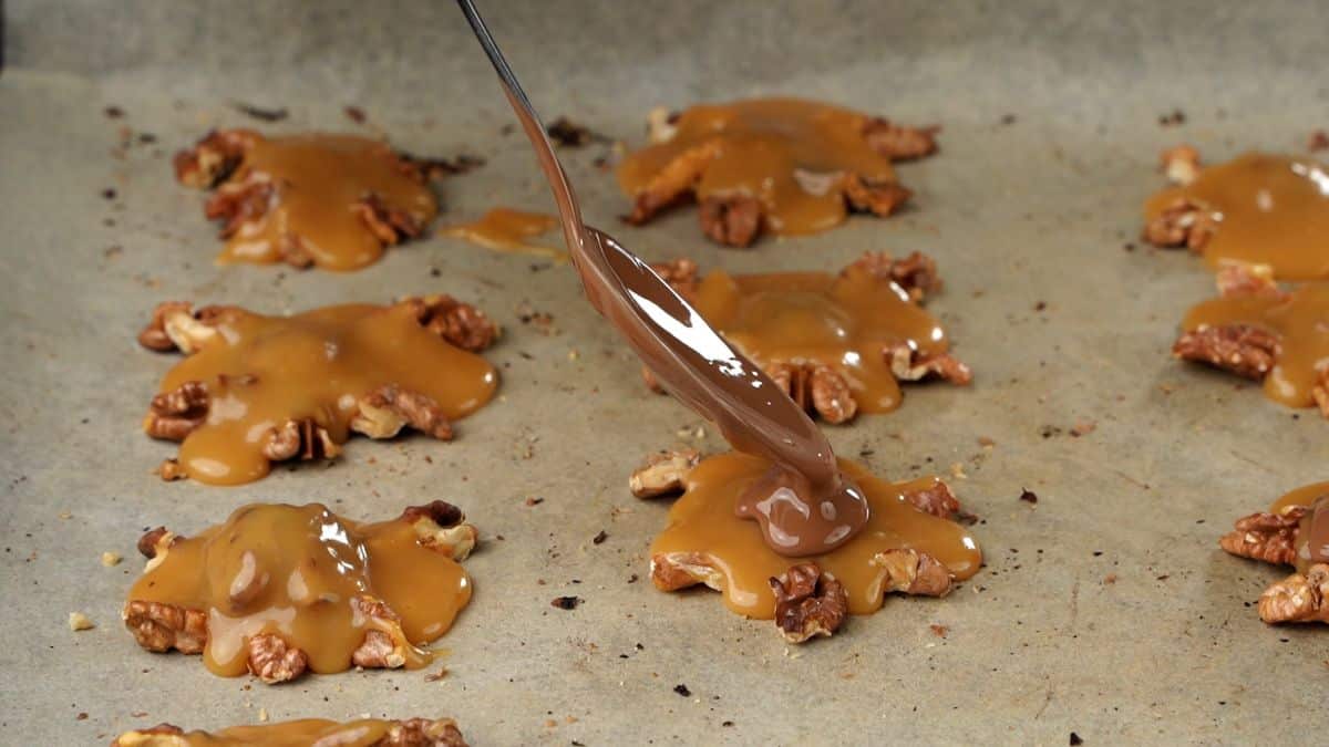 spoon of chocolate going on top of caramel on walnuts on parchmentp aper lined baking sheet