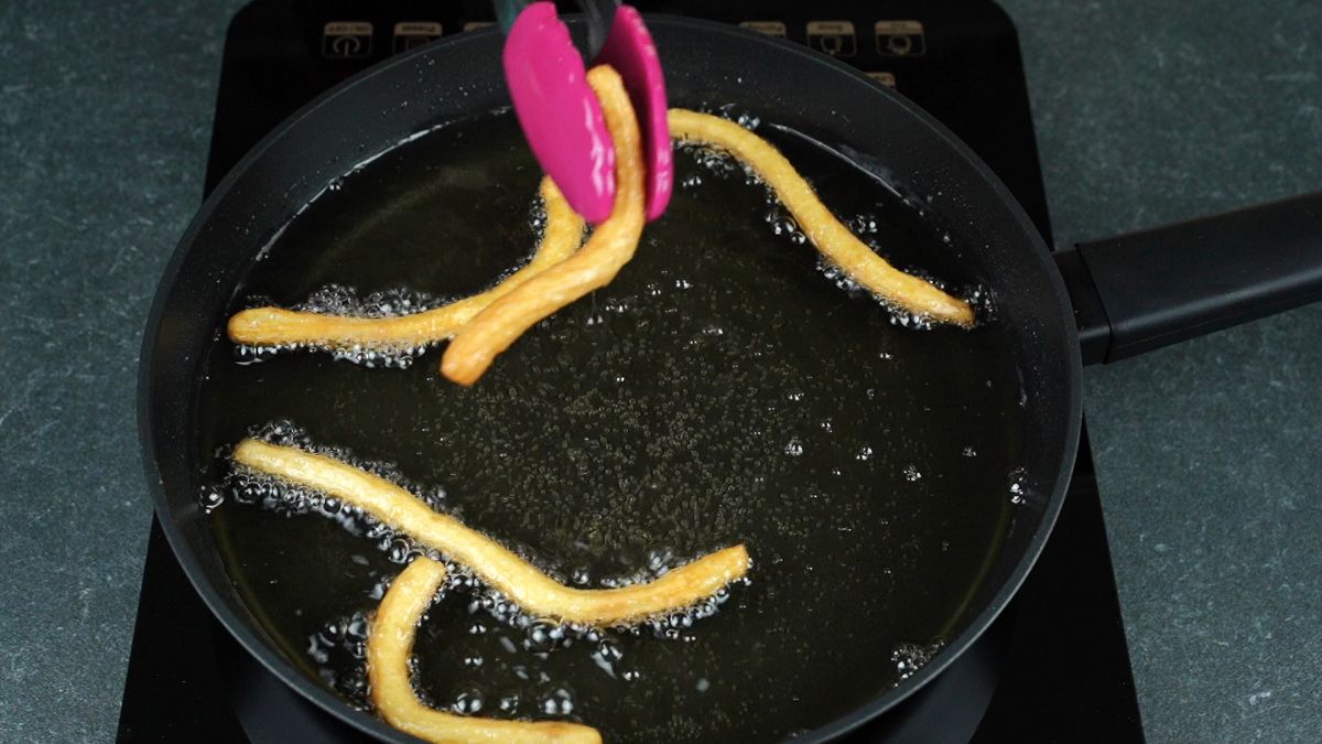 pink tongs pulling churros out of hot oil in skillet