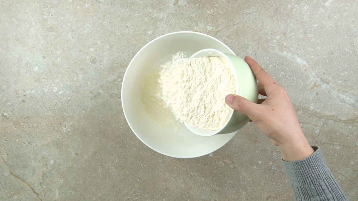 hand pouring flour into large white bowl