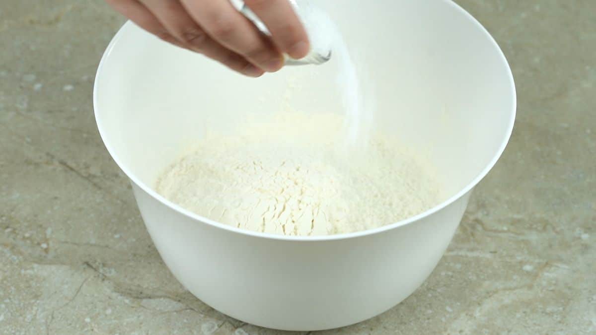 salt being poured into white bowl of flour