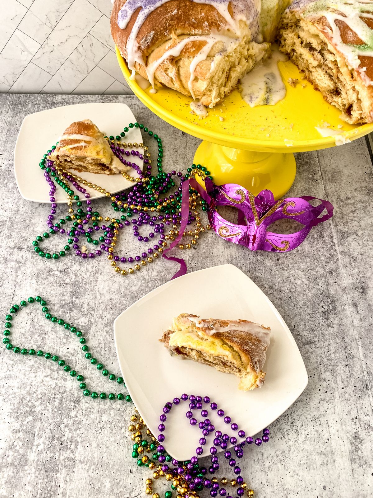 two plates of cake in front of yellow cake stand holding king cake