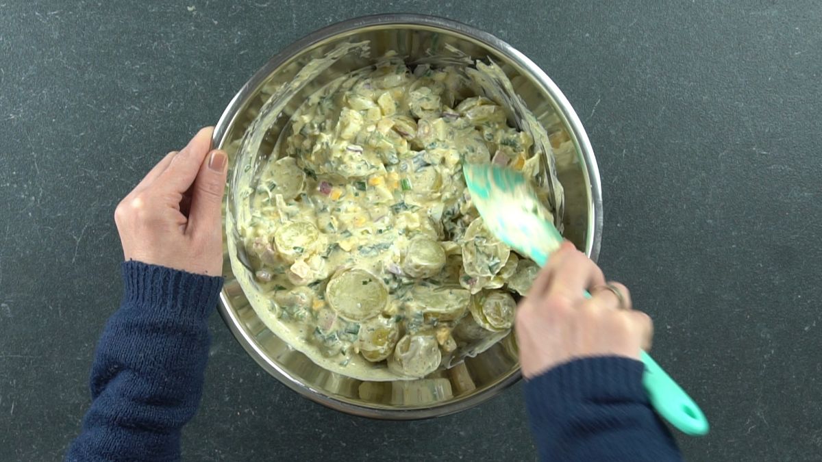 large silver bowl of potato salad being stirred