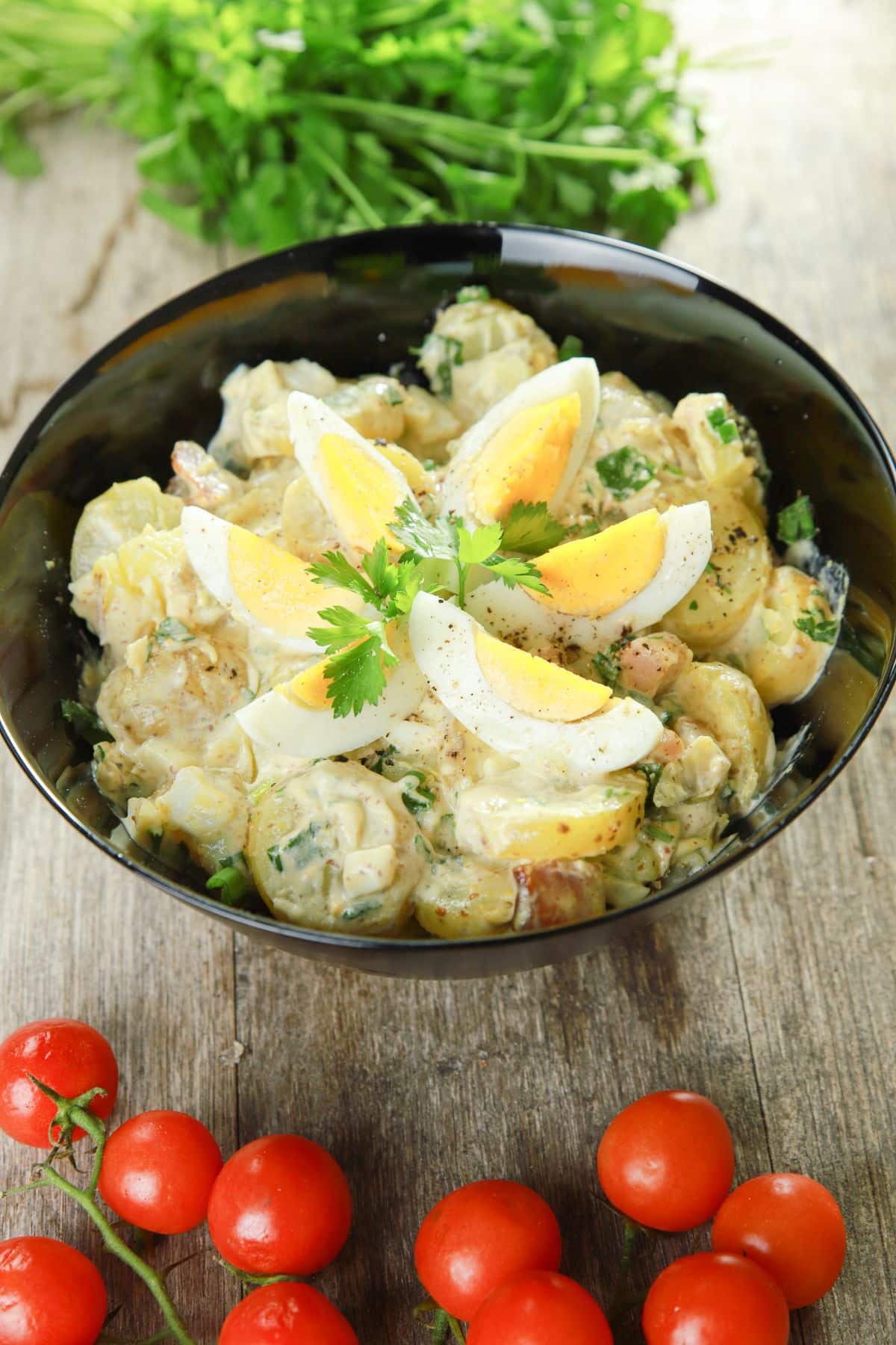black bowl of potato salad by cherry tomatoes and fresh herbs