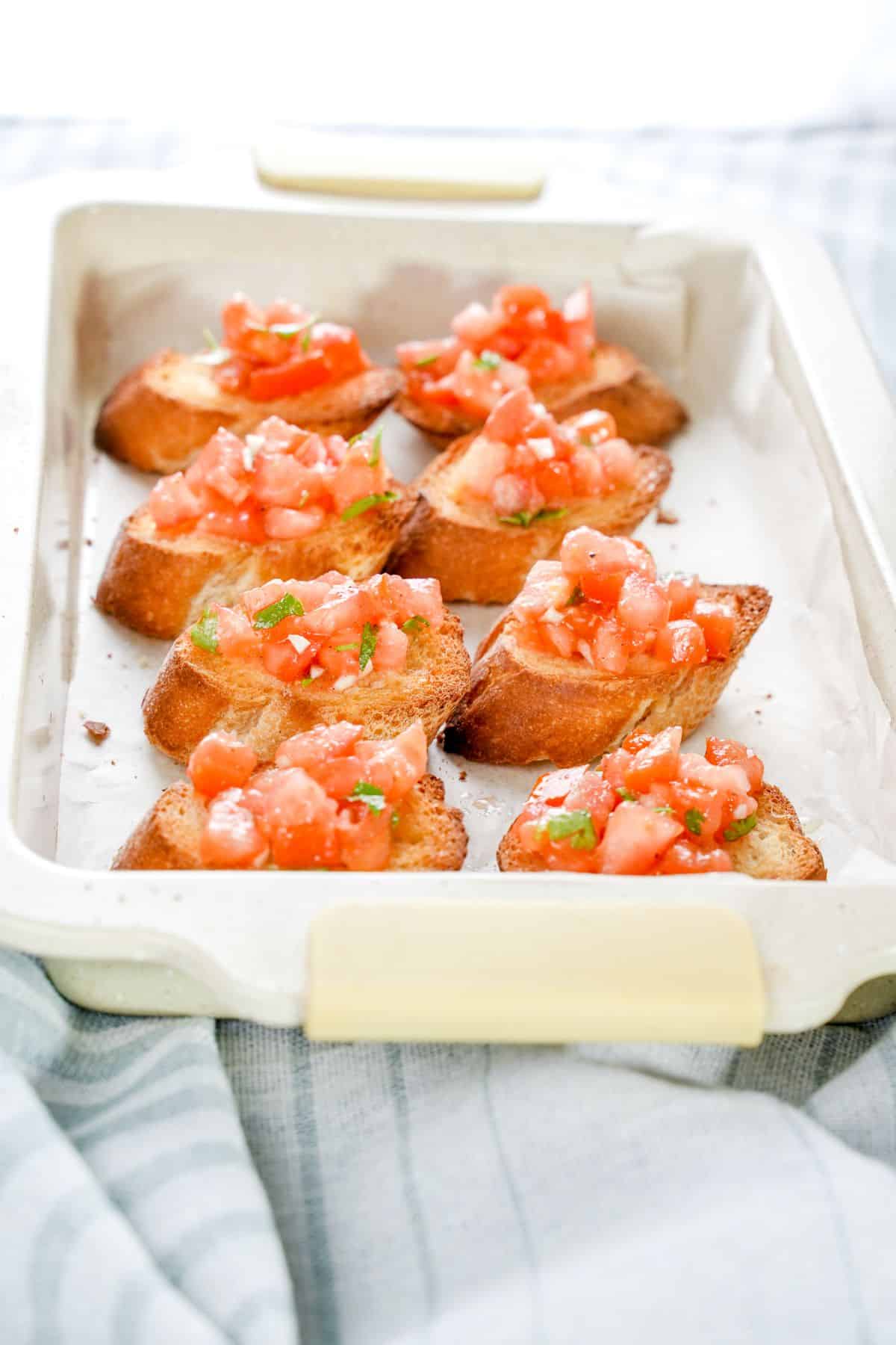 white baking dish filled with bruschetta sitting on gray towel