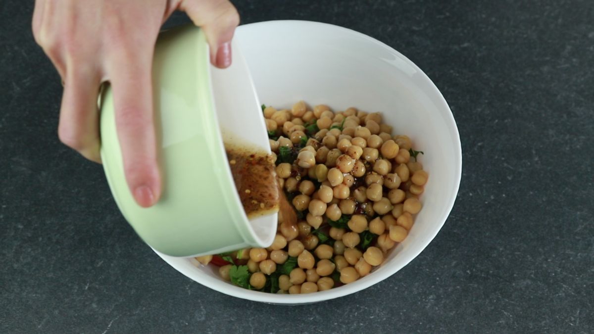 dressing being poured into bowl with chickpeas