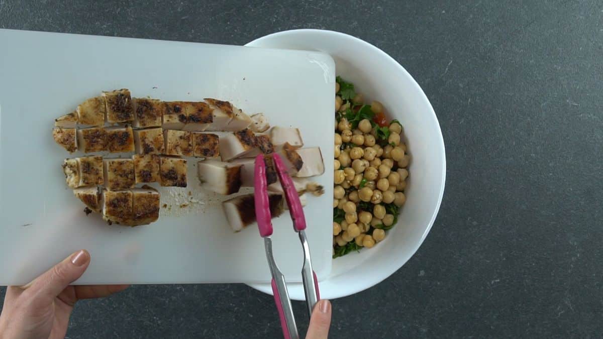 pink tongs putting chicken chunks into bowl of chickpeas