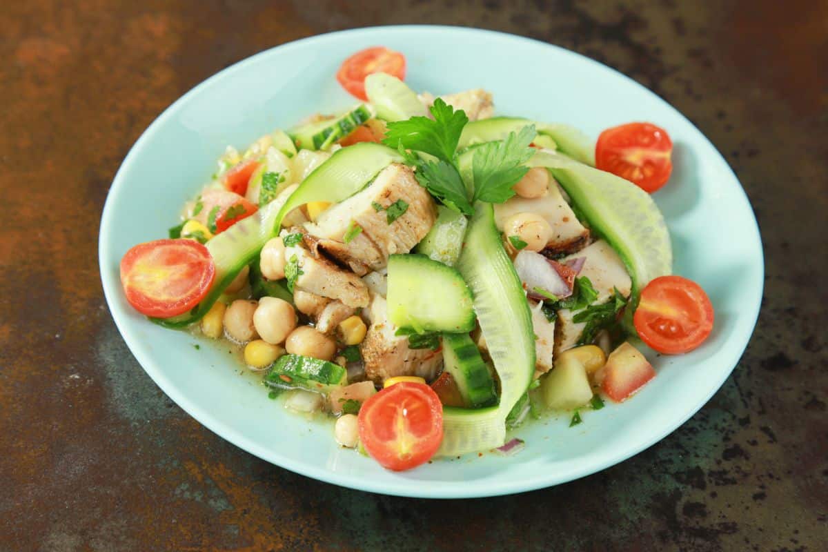 small round light blue plate of chickpea salad with shaved cucumber and cherry tomatoes on sides