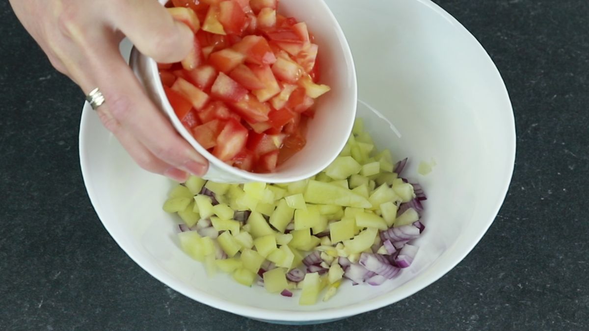 white bowl of tomatoes being poured into larger white bowl