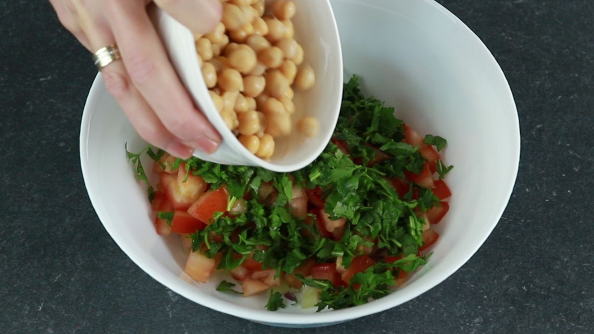 chickpeas being poured into bowl with other vegetables
