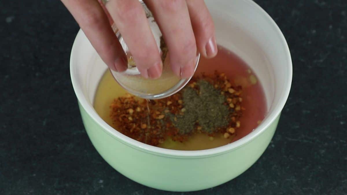 spices being added to bowl of dressing