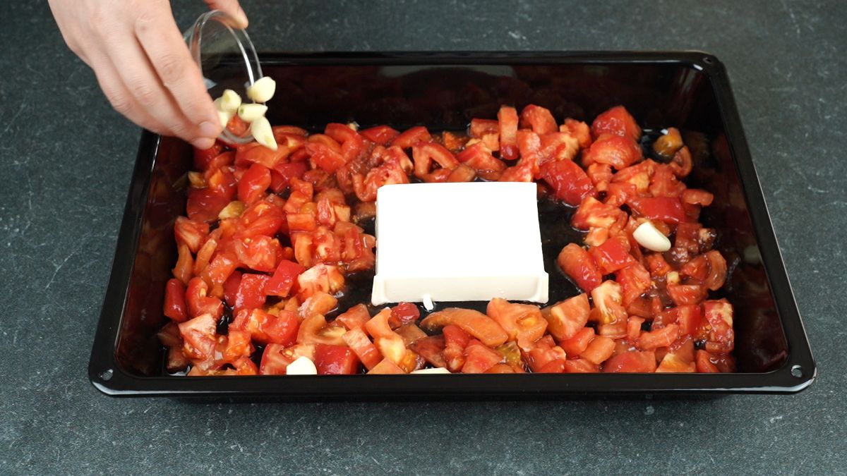 garlic cloves being added to baking sheet with tomatoes