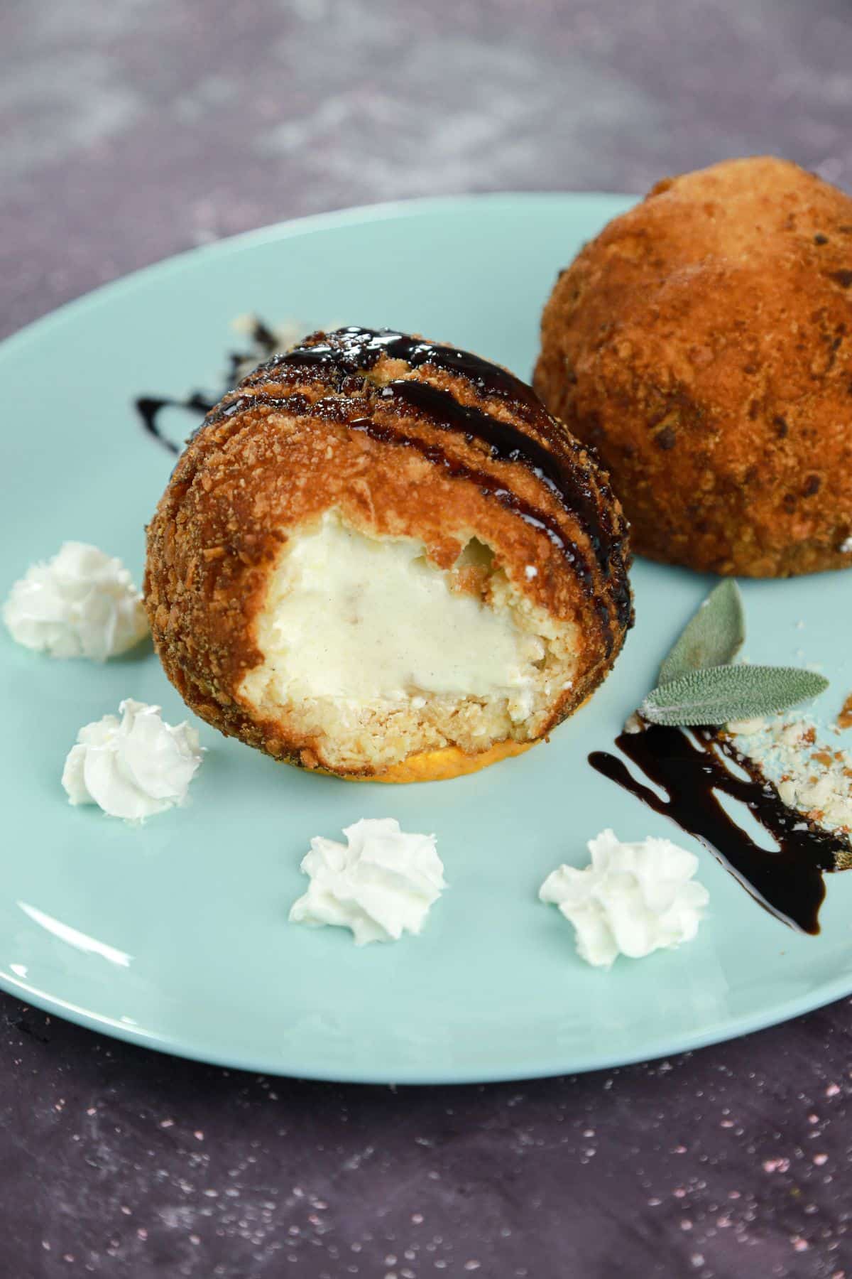 two fried ice cream balls on plate with syrup and whipped cream
