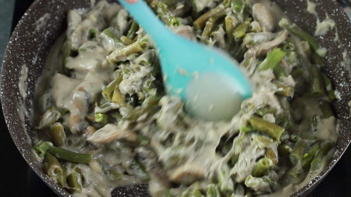 blue spoon stirring green beans into mushroom gravy