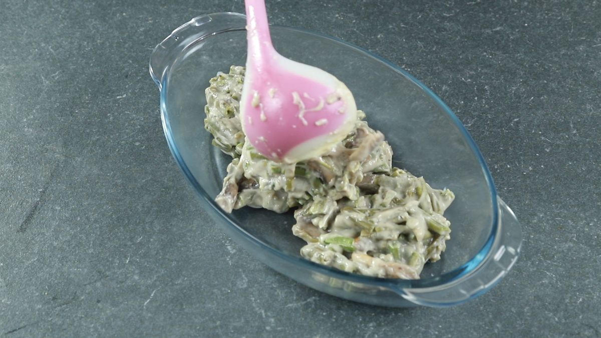 pink ladle scooping green beans into casserole dish