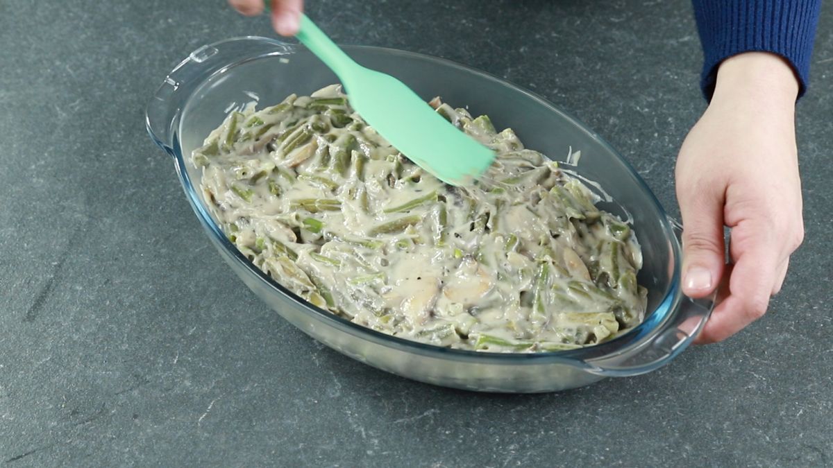 teal spatula spreading green beans and mushrooms into glass casserole dish