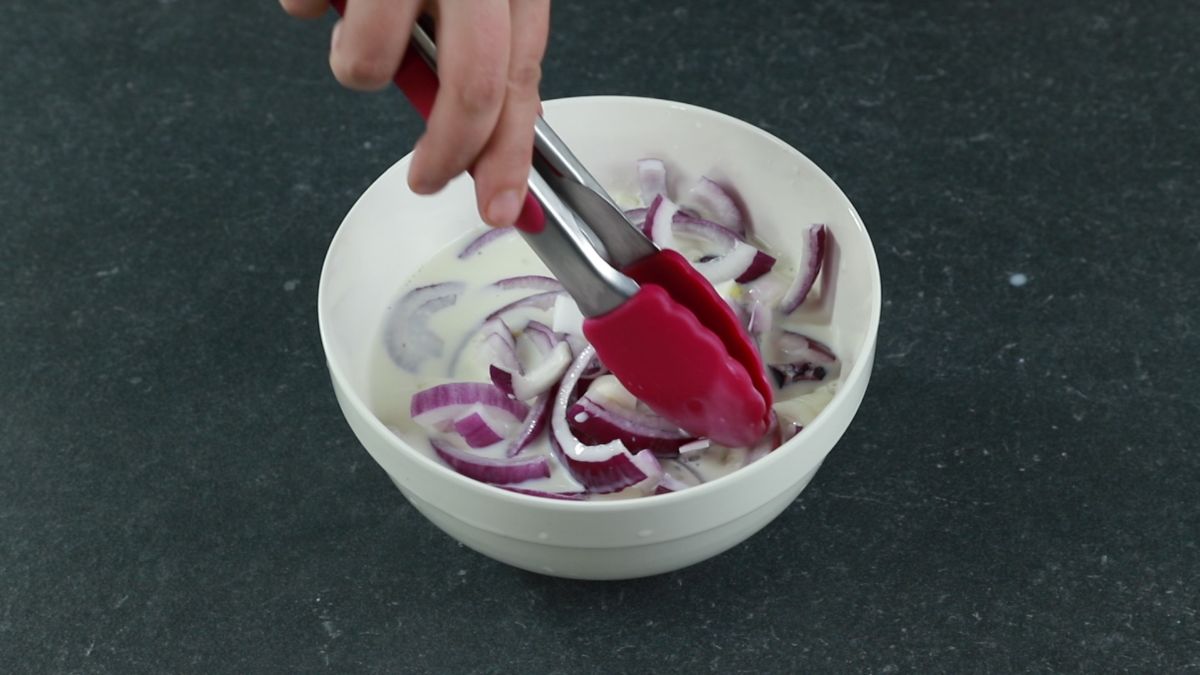 pink tongs dunking onions into milk
